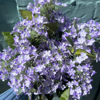 Artificial Lilac Charlotte Spray from Lotus Imports Ltd, single stem with delicate purple blossoms and green leaves.