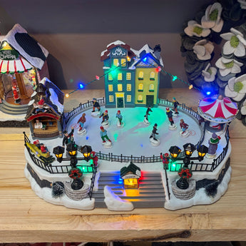Crystal World Christmas Village Ice Rink Light Up Ornament featuring a festive winter scene and glowing lights.