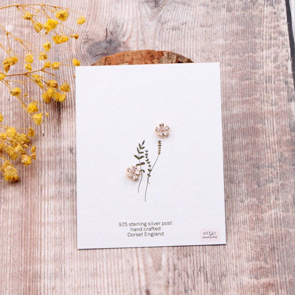 Gold earrings featuring crystal five-petal flower design by Attic Creations, showcased on a white background.