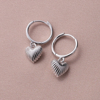 Silver hoop earrings with engraved heart-shaped designs, featuring debossed detail, by Attic Creations.